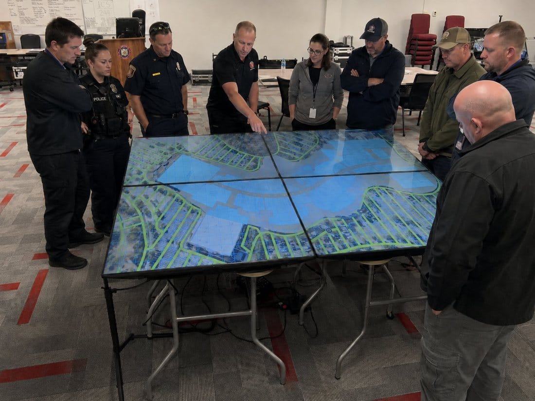 Law enforcement, fire, and EMS responders training around a Counterstrike Terrain Large display showing an aerial map